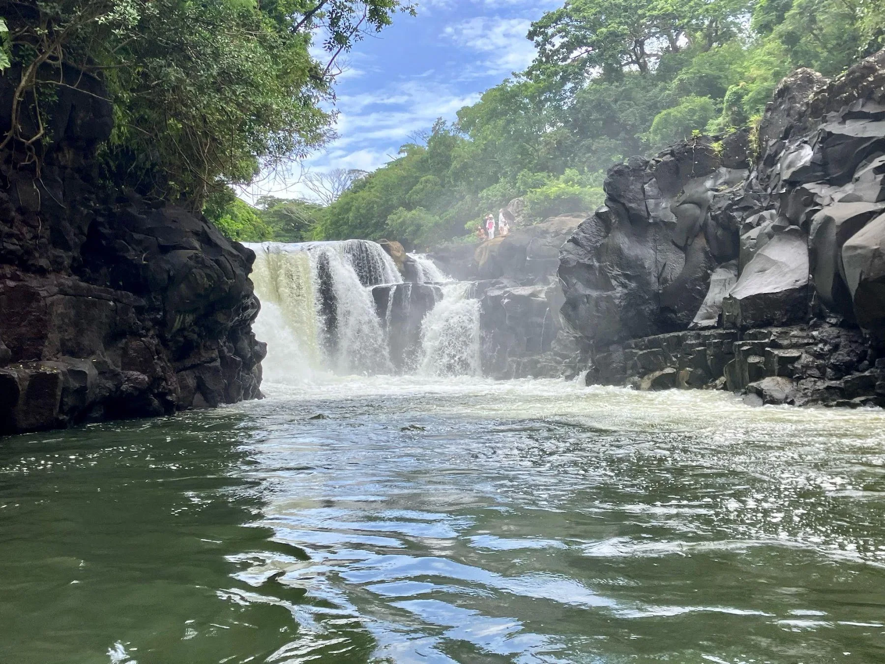 A waterfall between wooded rocks viewed from the water